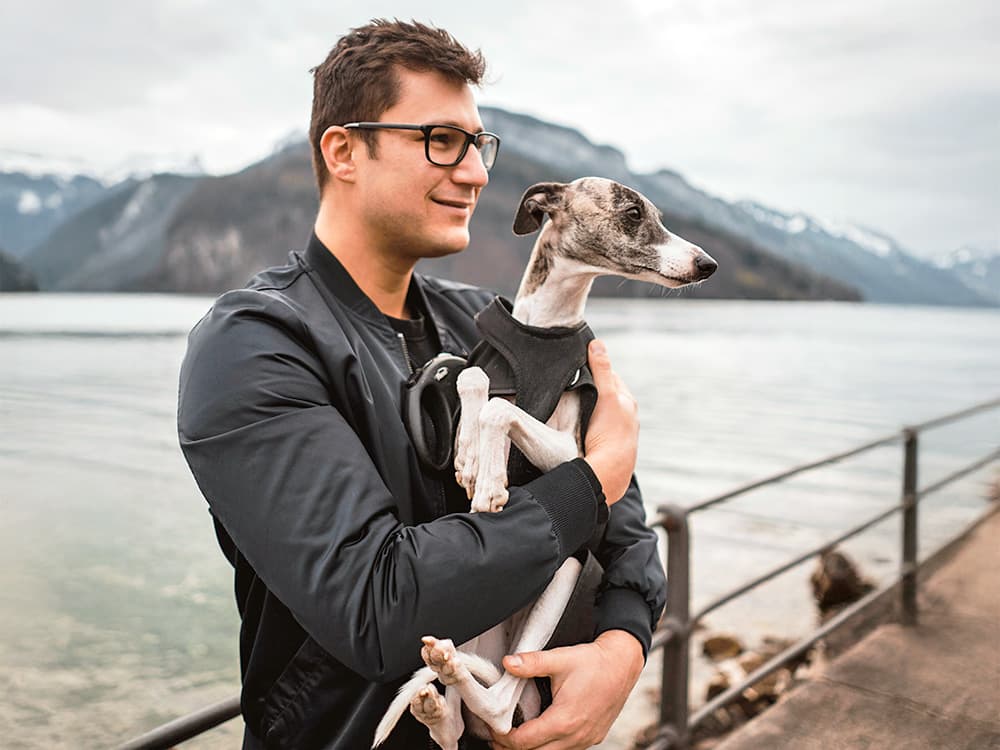 Man holding his Whippet dog outside.